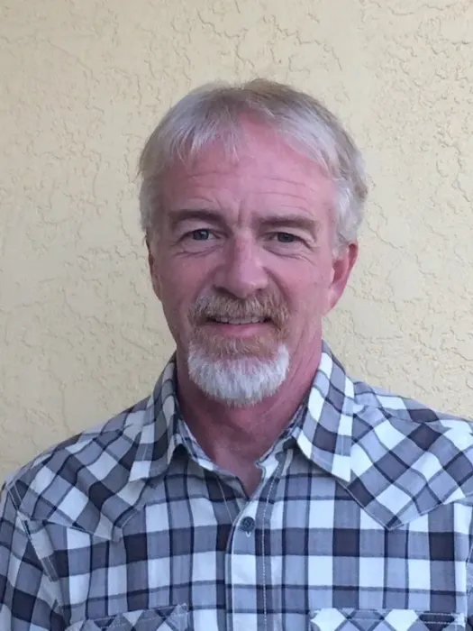 A man with a beard is wearing a plaid shirt and smiling.