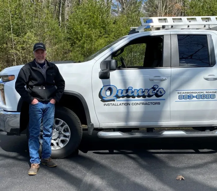A man is standing in front of a truck that says quinn 's