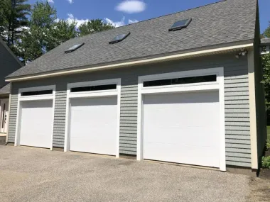 A garage with three white garage doors and a gray roof.