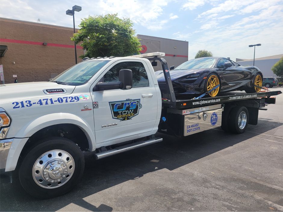 A white tow truck is towing a black sports car.
