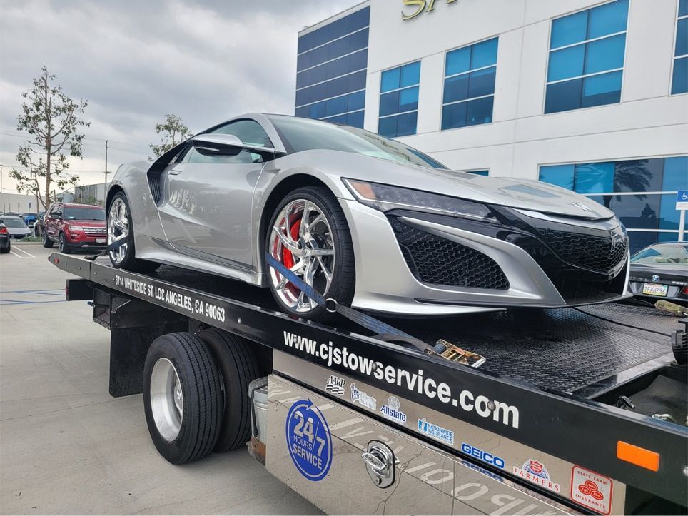 A silver sports car is sitting on top of a Cj’s Tow Service Truck.