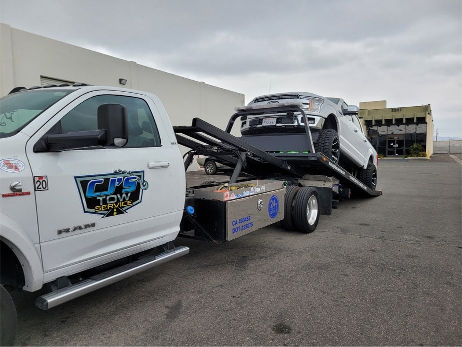 A white tow truck is towing a white truck in a parking lot.