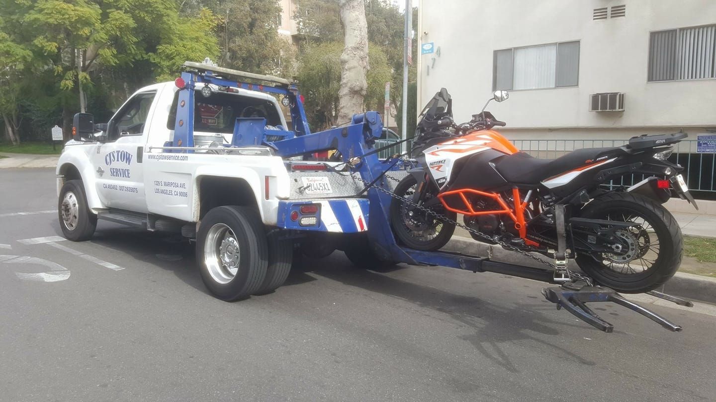 A tow truck is towing a motorcycle down the street.