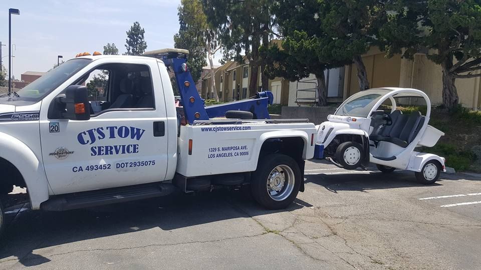 A tow truck is towing a golf cart in a parking lot.