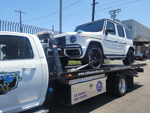 A white mercedes benz g63 is being towed by a tow truck.