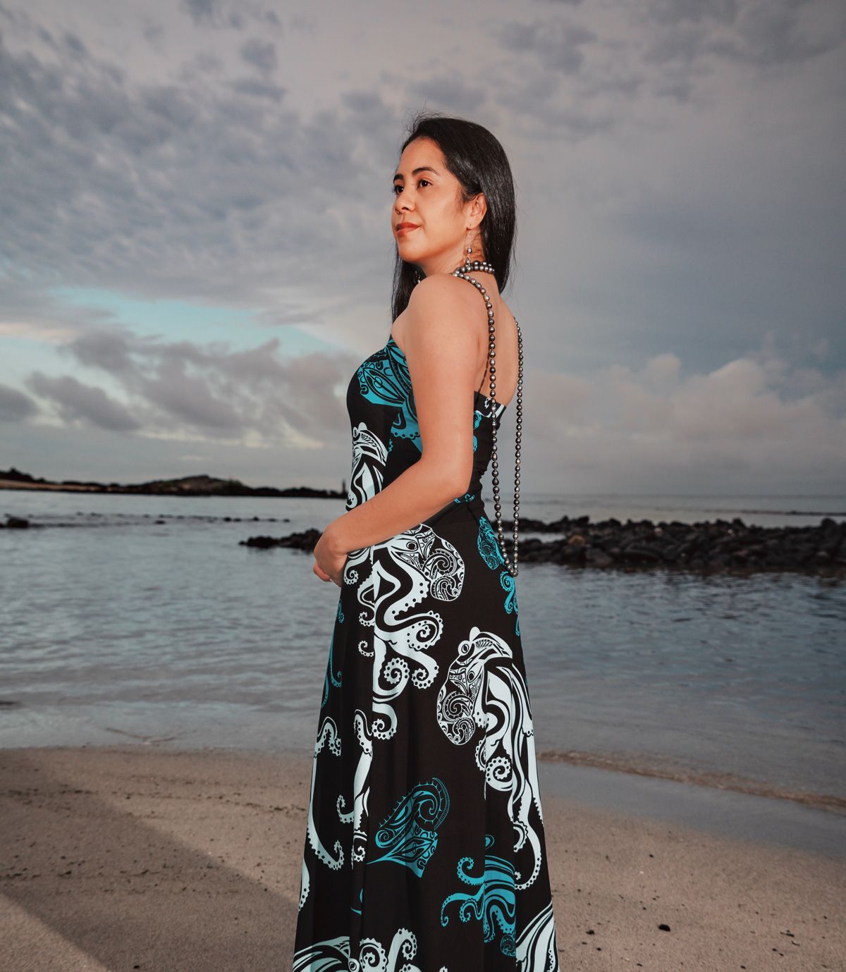 A woman in a black and blue dress is standing on a beach