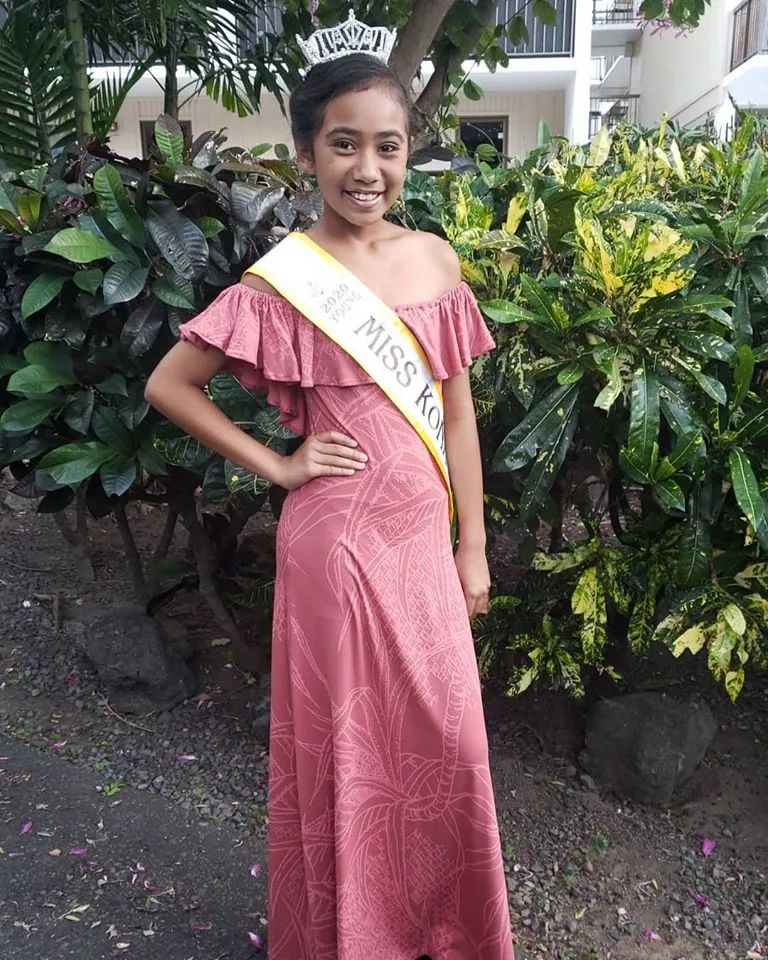 A girl in a pink dress is wearing a sash that says miss hawaii