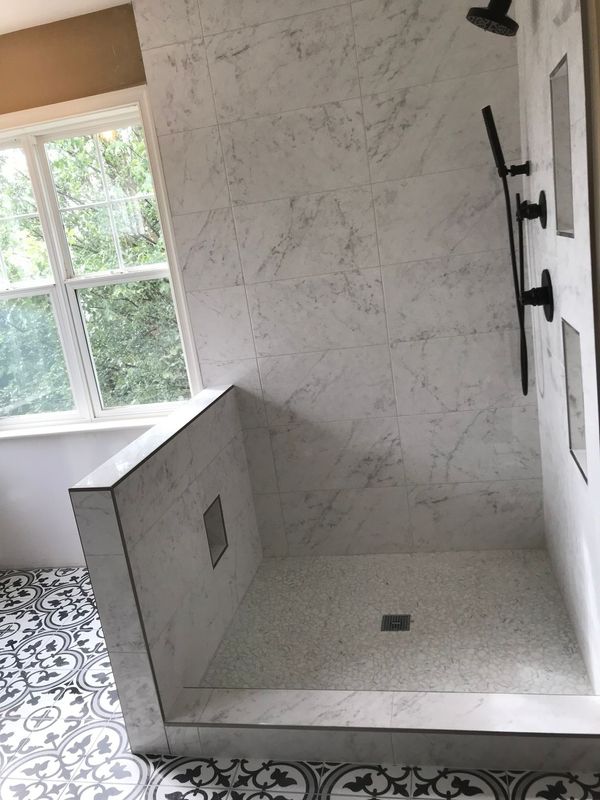 Shower with textured white walls, black fixtures, and mosaic floor. A window is in the background.