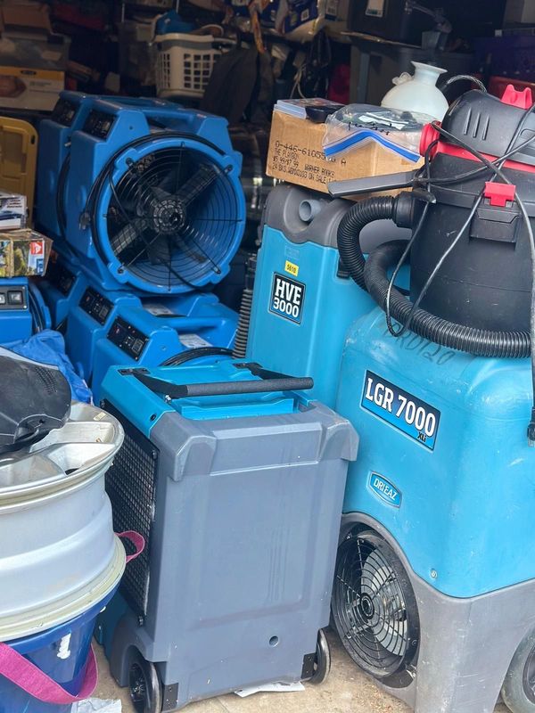 Blue air movers and a vacuum for water damage restoration equipment inside a storage area.