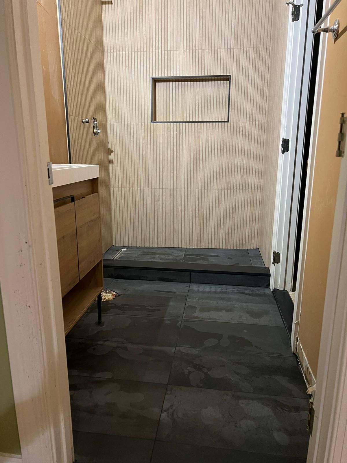 Bathroom remodel with dark gray floor tiles and light vertical wall tiles; shower entrance.