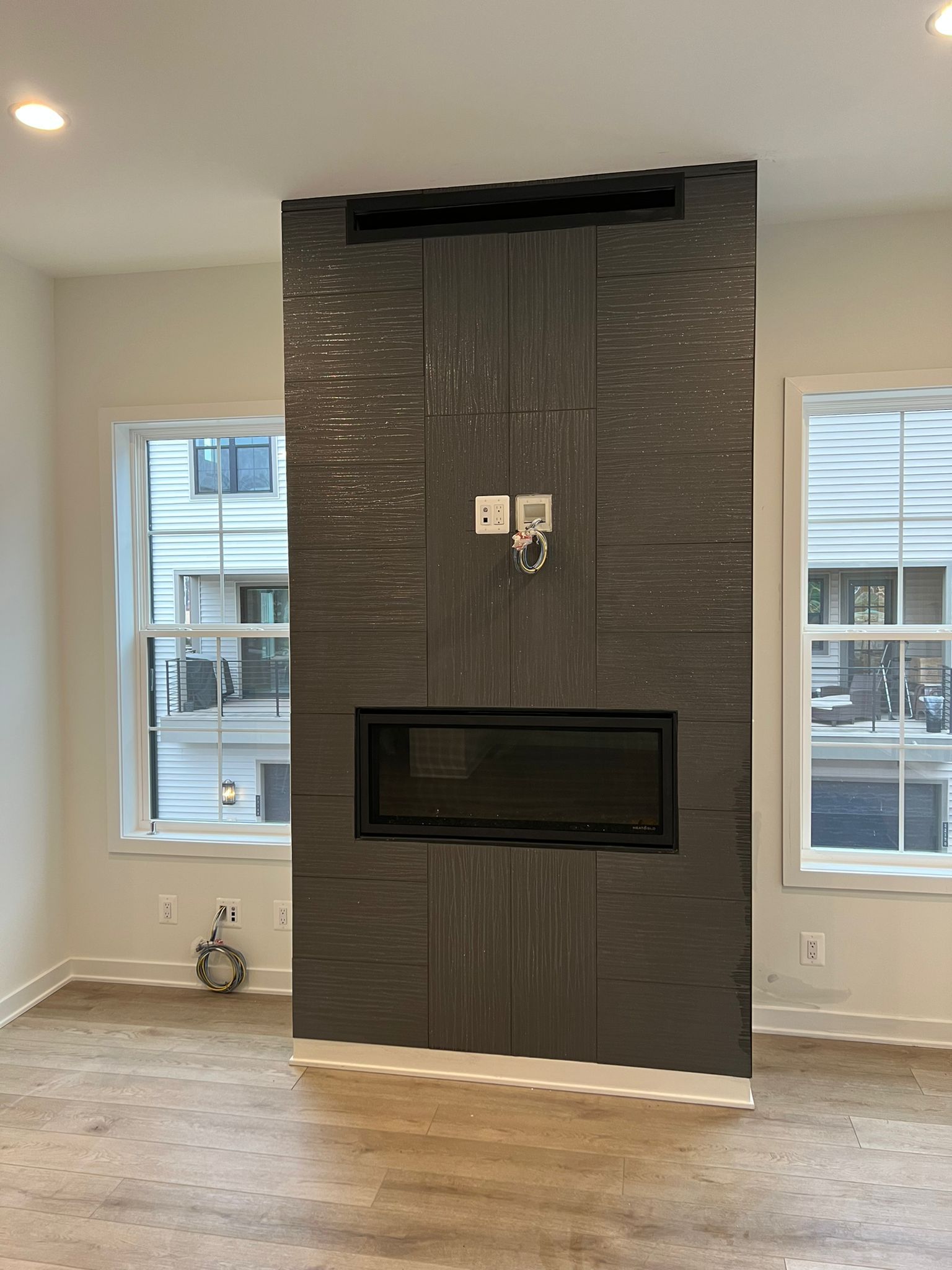 Fireplace with dark textured tile in a room with two windows.
