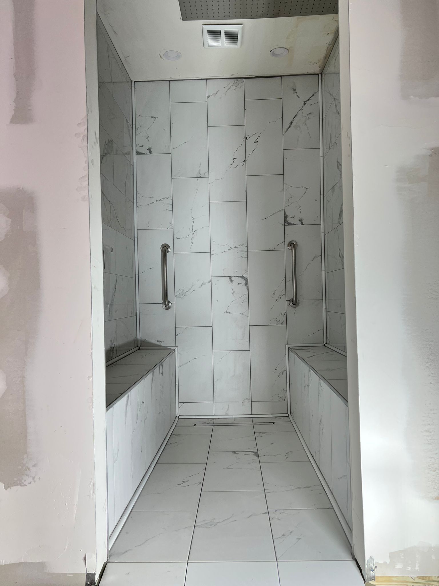 A shower under construction with tile walls, built-in benches, and grab bars.