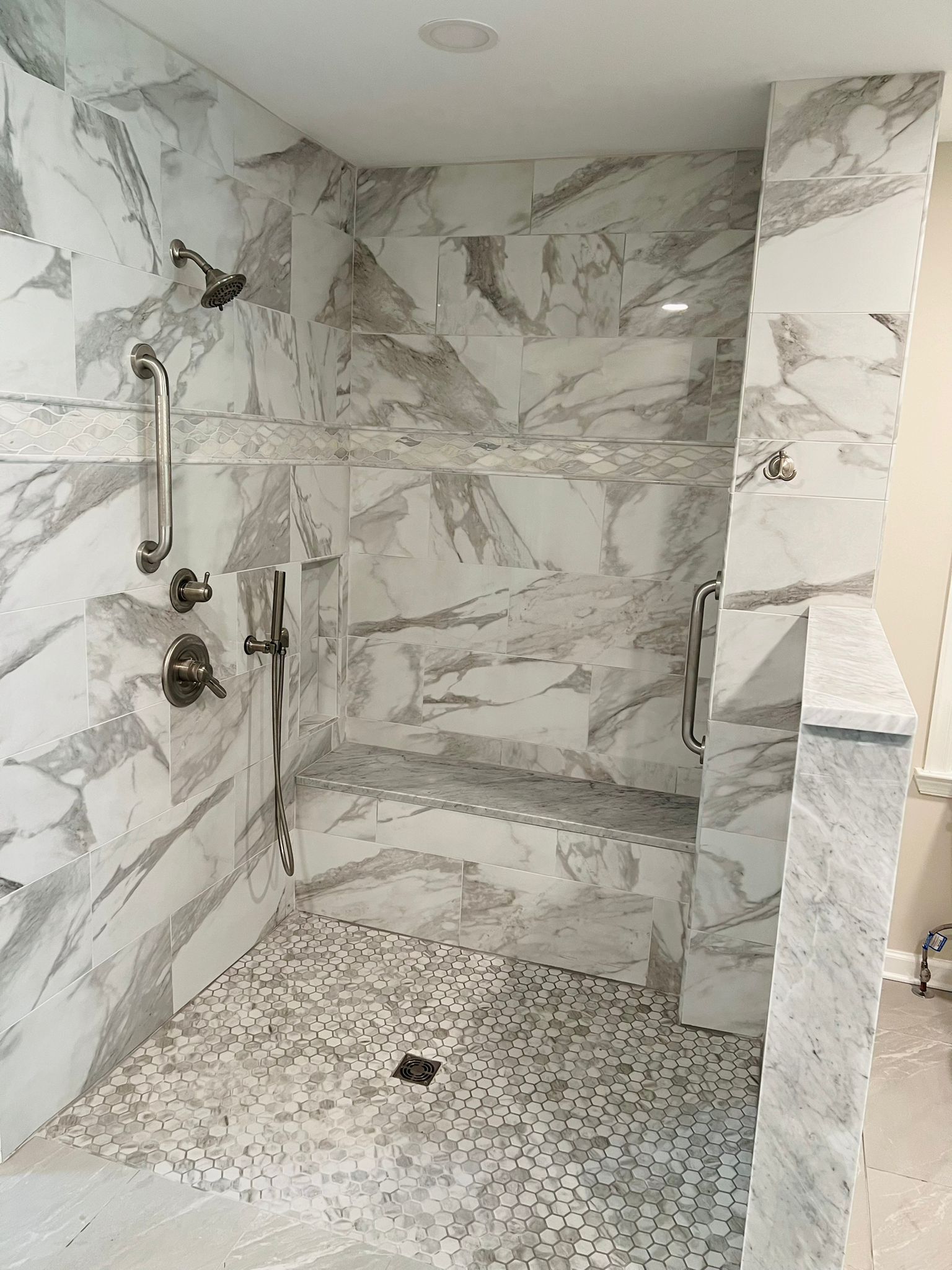 Walk-in shower with gray and white marble tiles, pebble floor, built-in bench, and multiple showerheads.