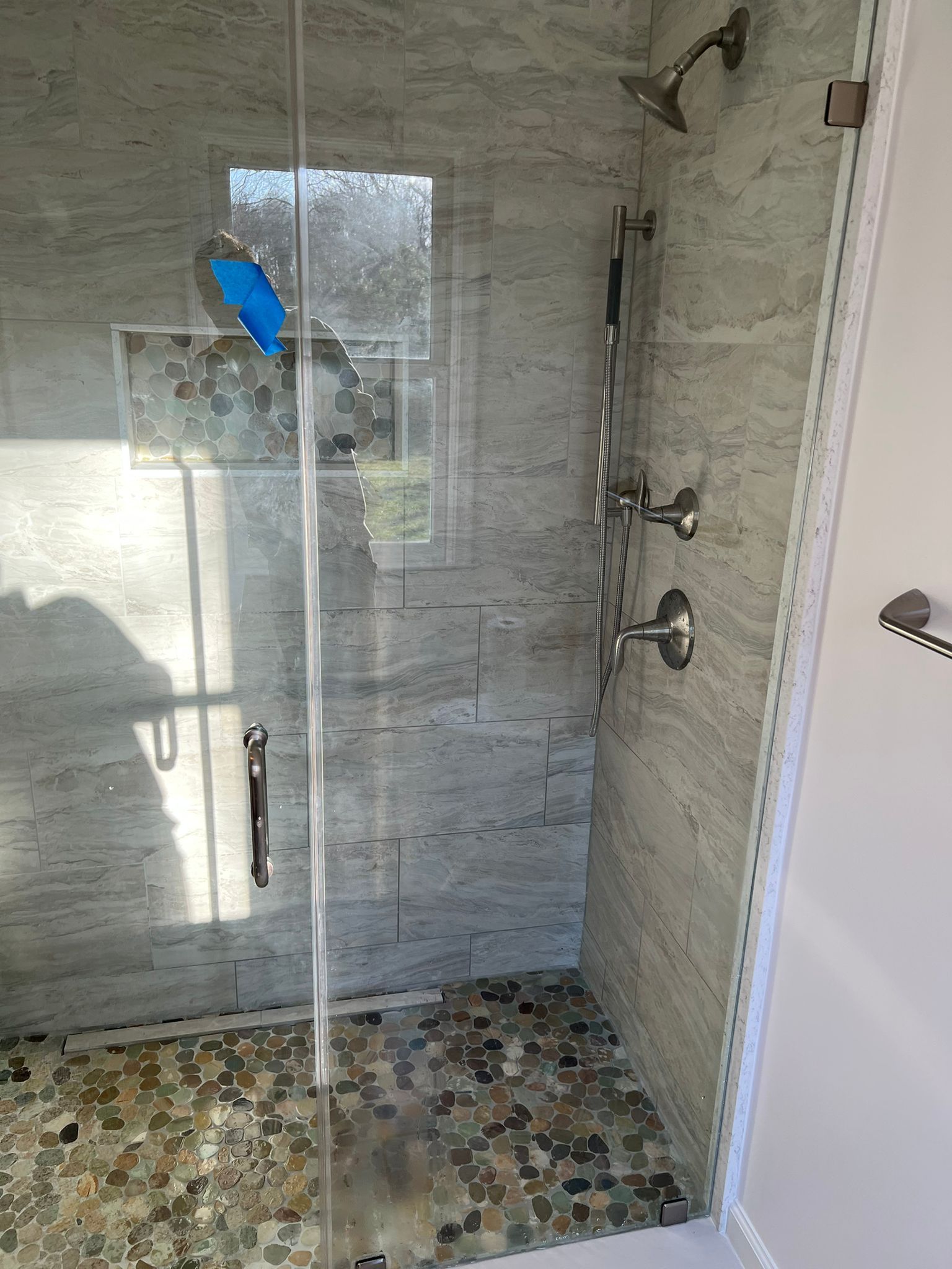Shower with glass door, stone tile walls and floor, and silver fixtures.