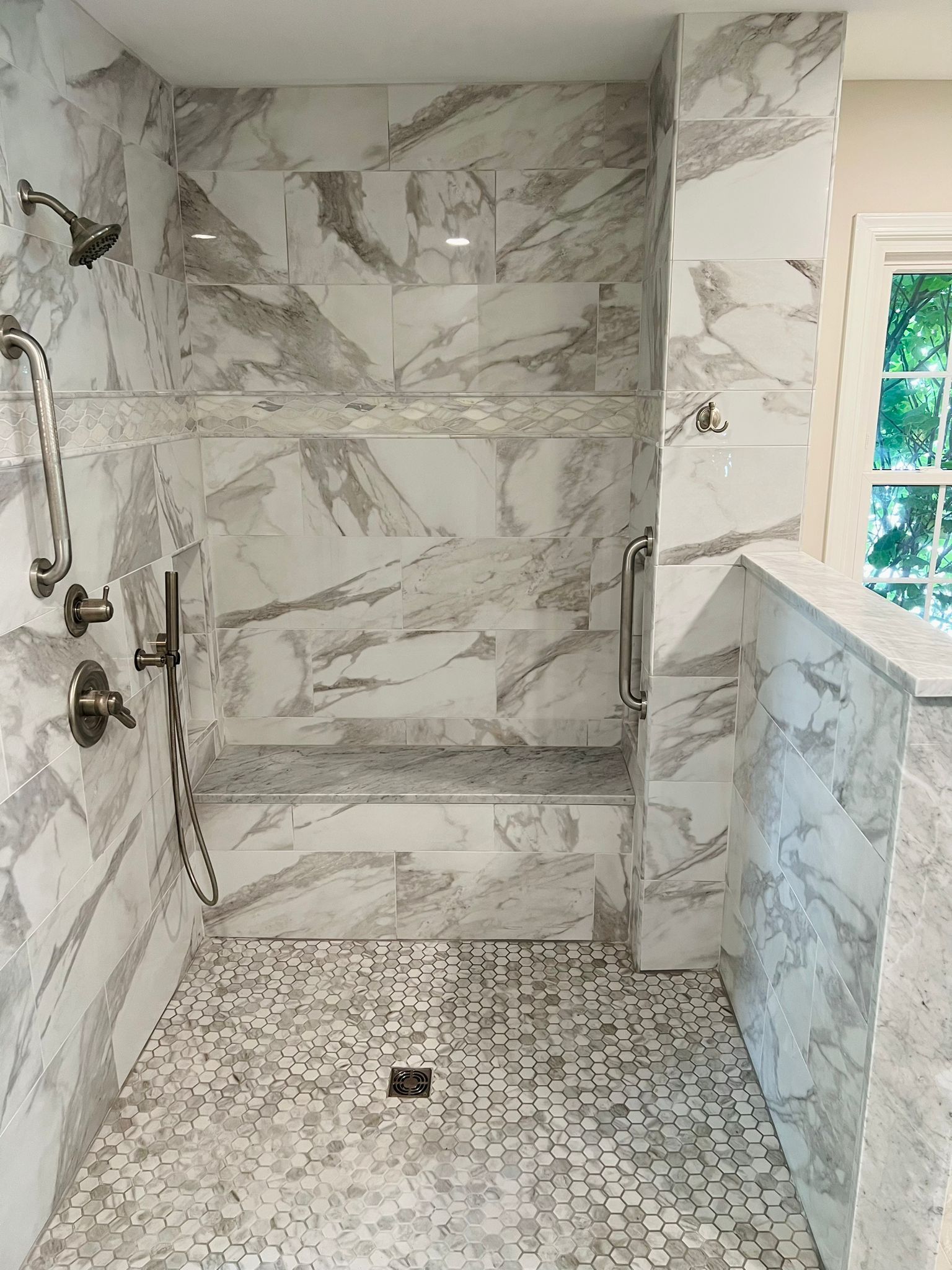 Marble-tiled shower with built-in bench, handheld shower head, and mosaic floor. Silver fixtures.