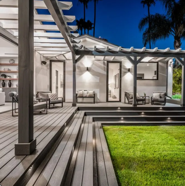 Outdoor patio with gray decking, pergola, and recessed lighting, overlooking a green lawn at night.