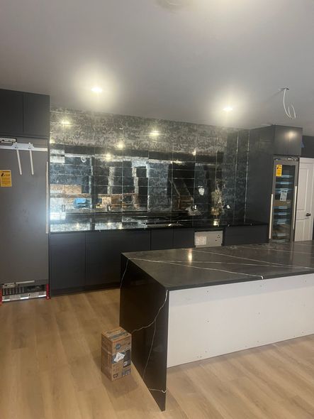 Modern kitchen with mirrored backsplash, black cabinets, white island, and wood floors.