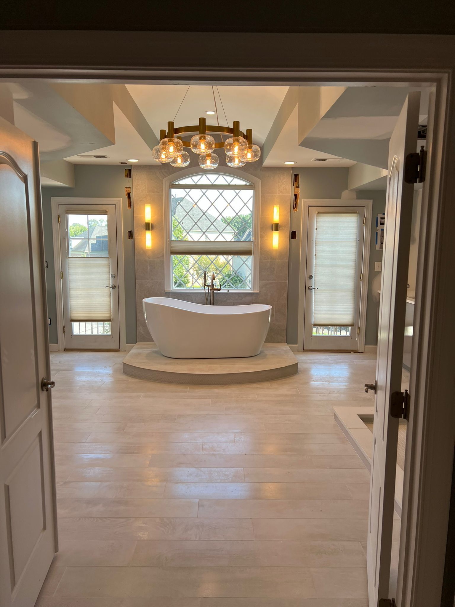 Spacious bathroom with white soaking tub, light-colored wood floors, and decorative chandelier.