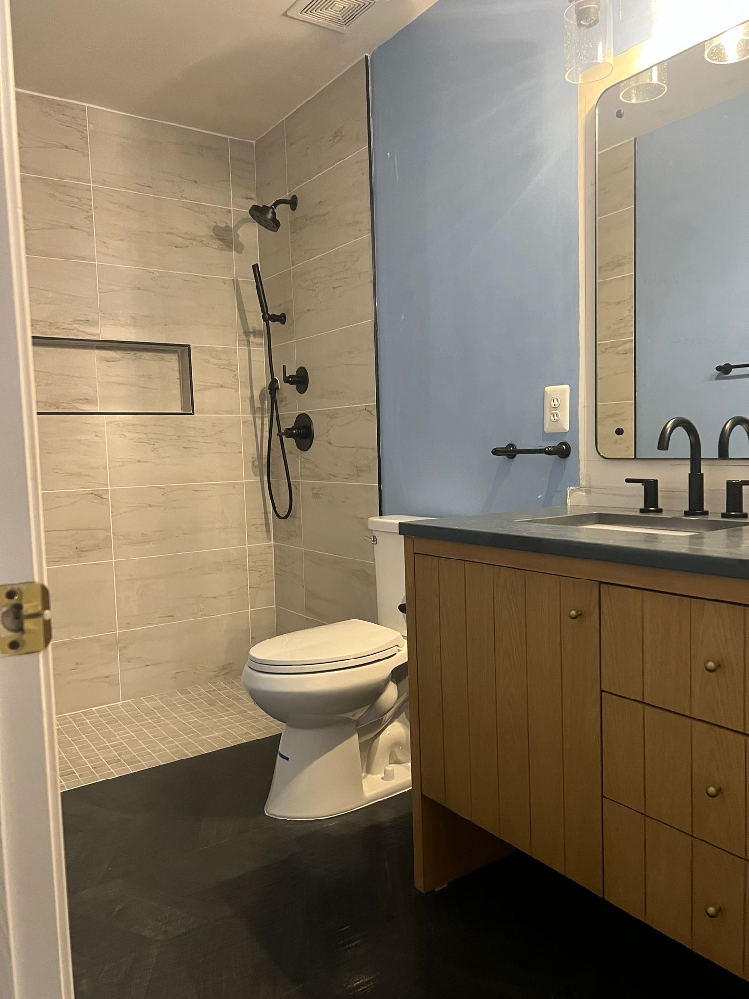 Bathroom with gray tile shower, blue wall, wooden vanity, black fixtures, and a toilet.