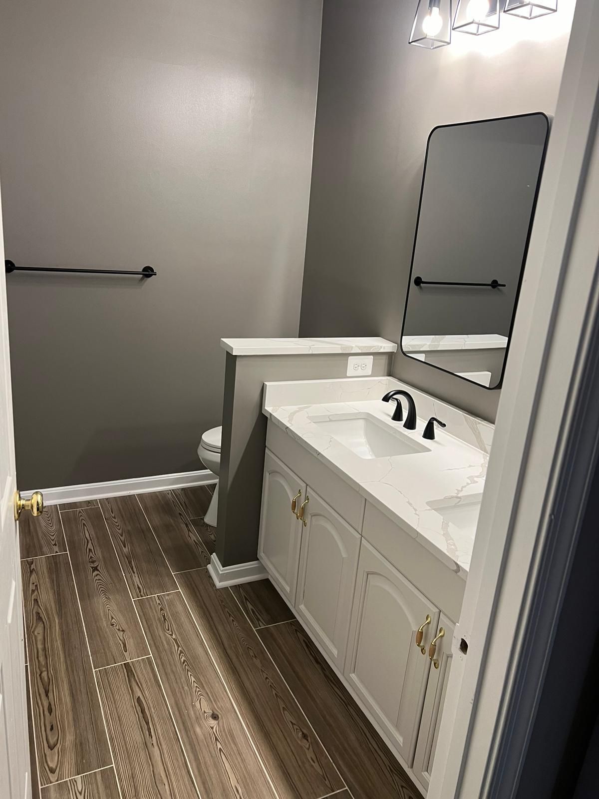 Bathroom with gray walls, white vanity, black fixtures, and wood-look tile flooring.