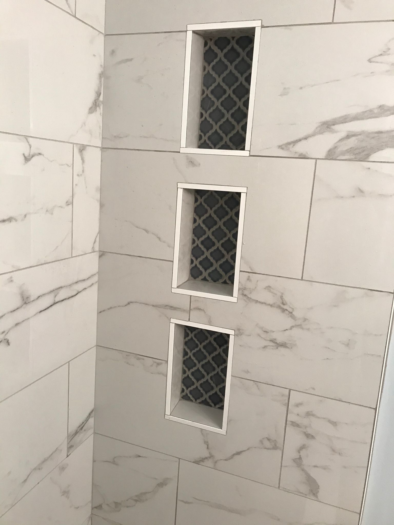 Tiled shower wall with three rectangular niches lined with patterned tile.