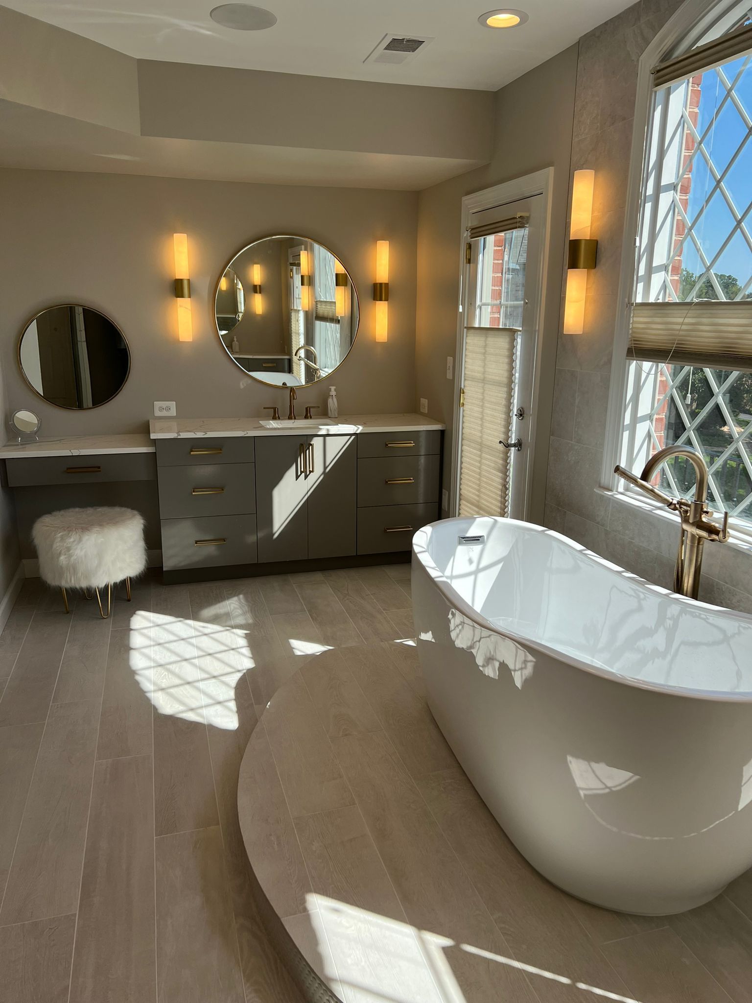 Luxurious gray and white bathroom with a freestanding tub, vanity, and large diamond-paned window.
