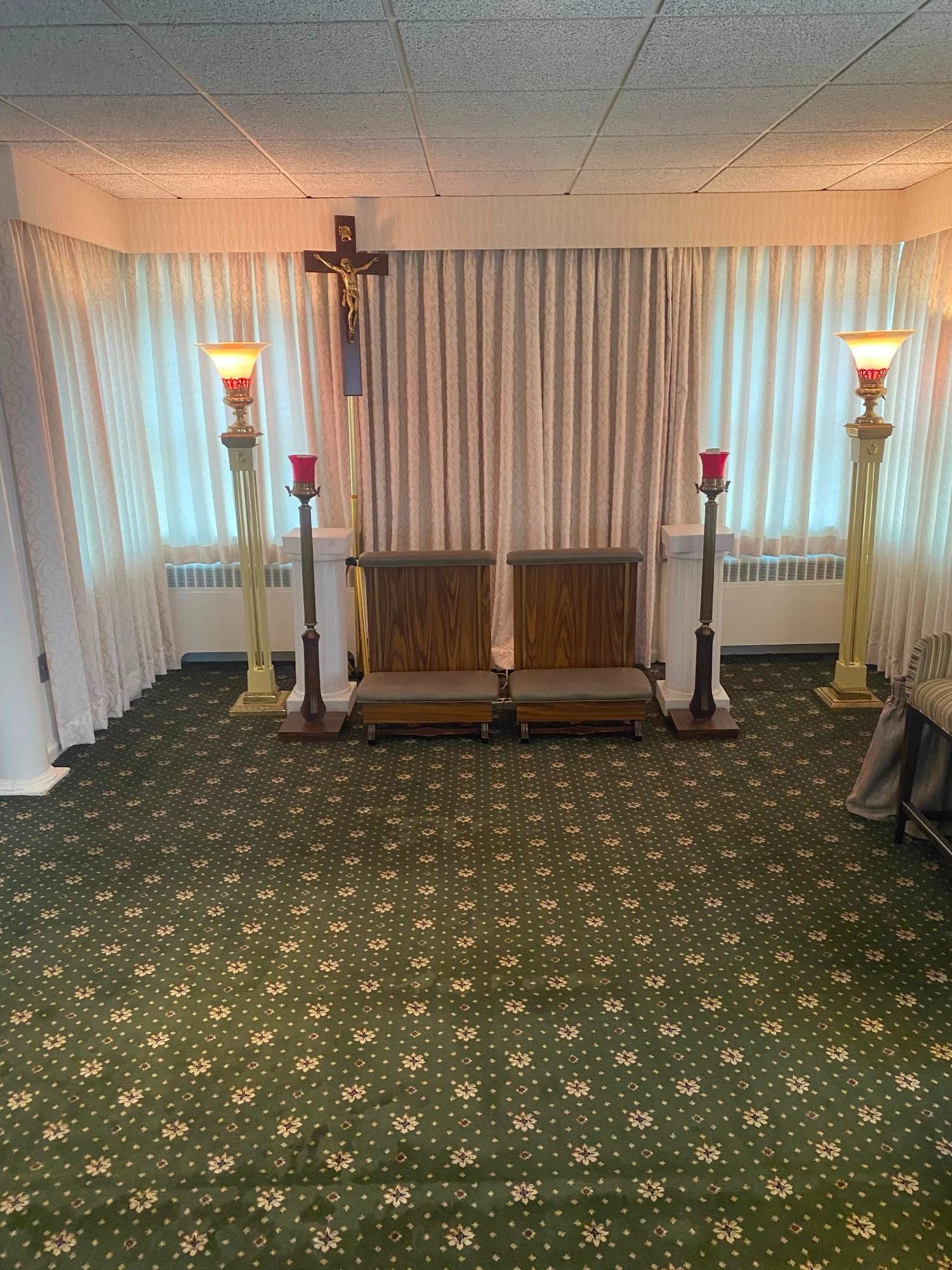 Funeral home chapel: a cross above two wooden pews, flanked by candle stands on a green carpet.