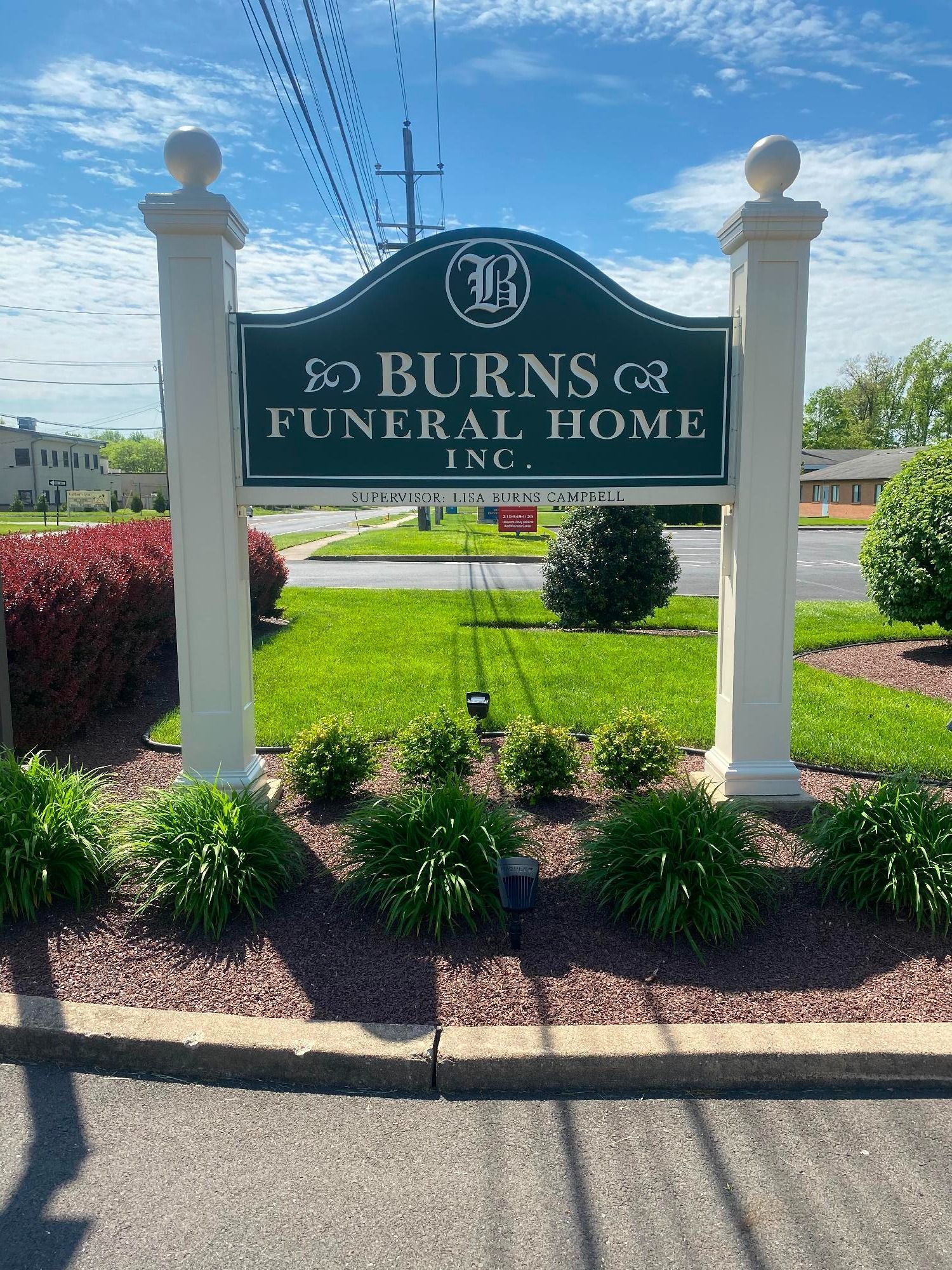 Sign for Burns Funeral Home, Inc. Green and white sign with logo, set in landscaped area.