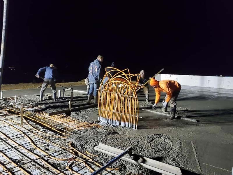 A group of construction workers are working on a concrete floor at night.