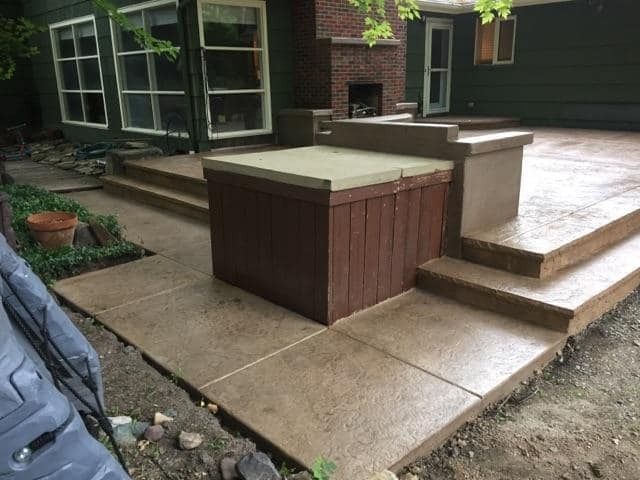 A concrete patio with stairs and a fireplace in the backyard of a house.