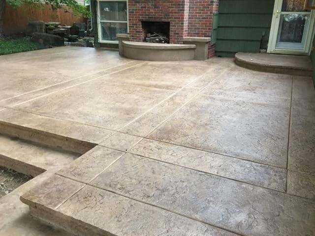 A concrete patio with stairs and a fireplace in the backyard.