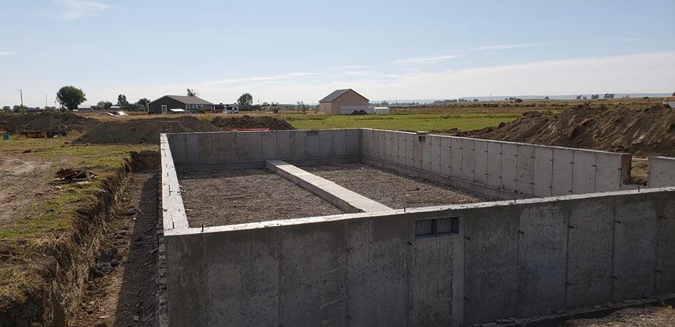 A large concrete wall is sitting in the middle of a dirt field.