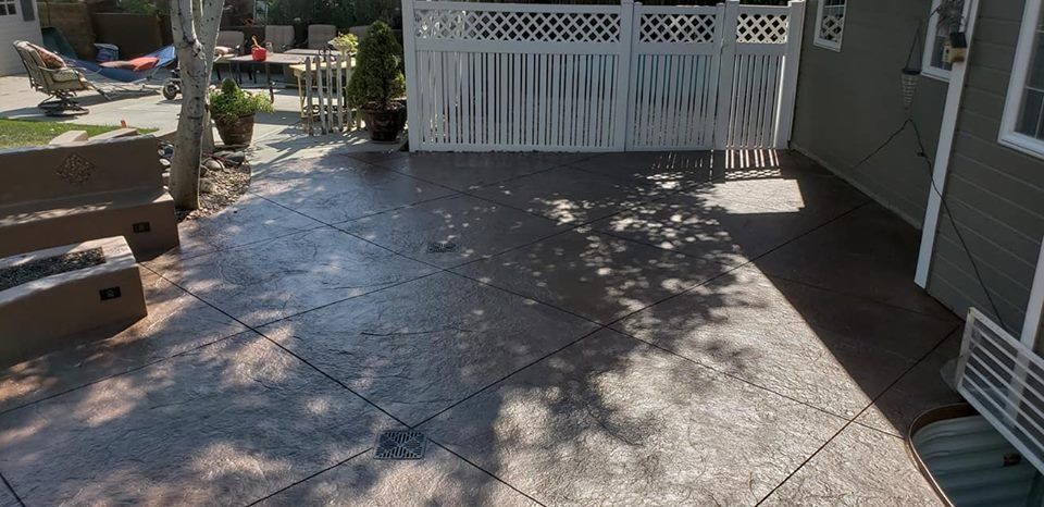 A patio with a fire pit and a white fence in the backyard of a house.