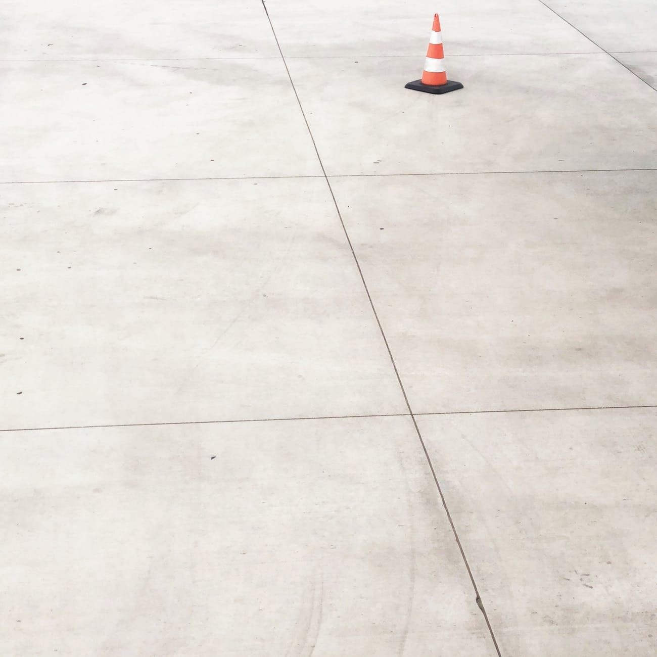 A red and white traffic cone is sitting on a concrete surface.