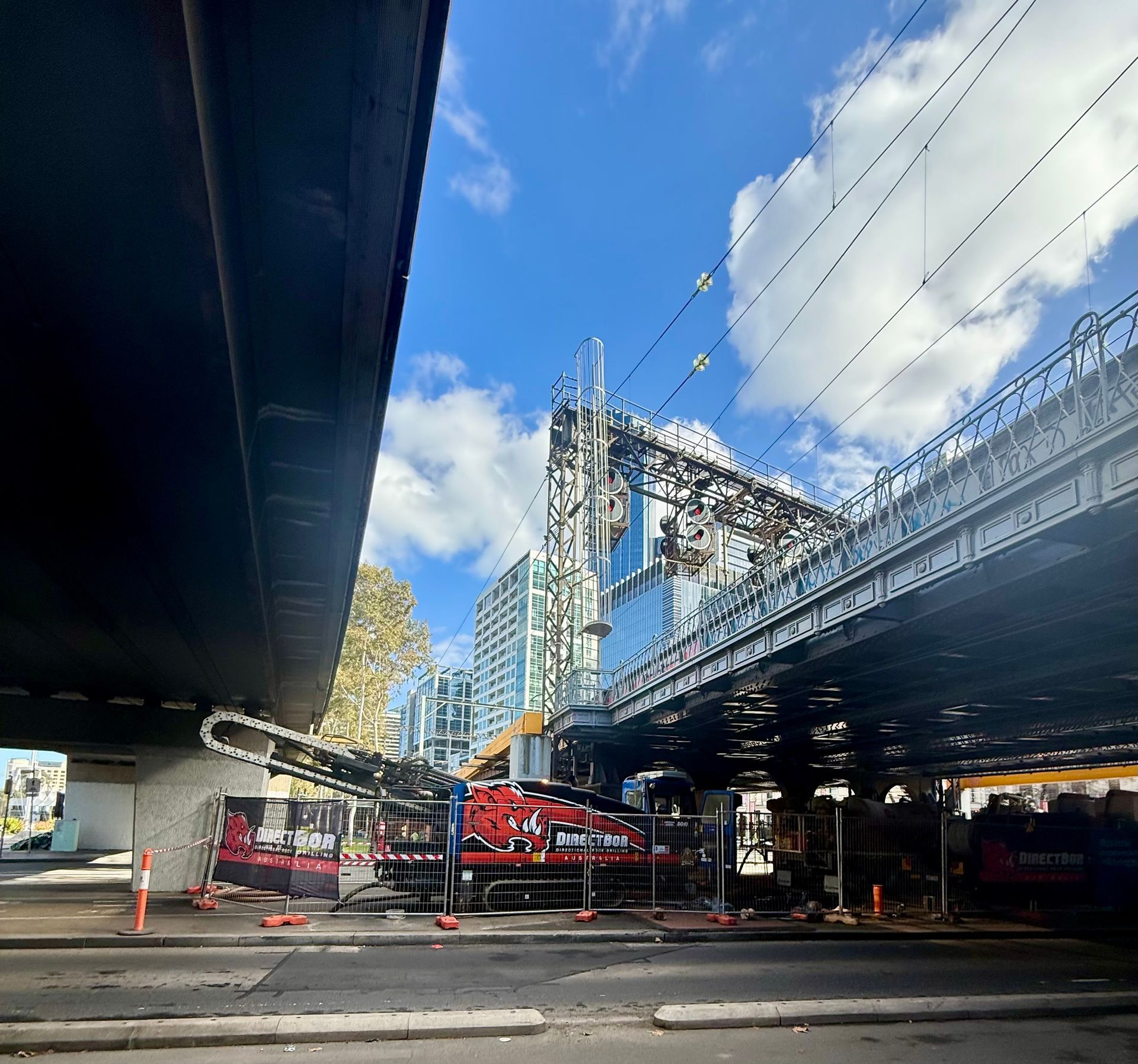 A worker operates a heavy machine to drill an underground pipe on a grassy area near a sidewalk edge