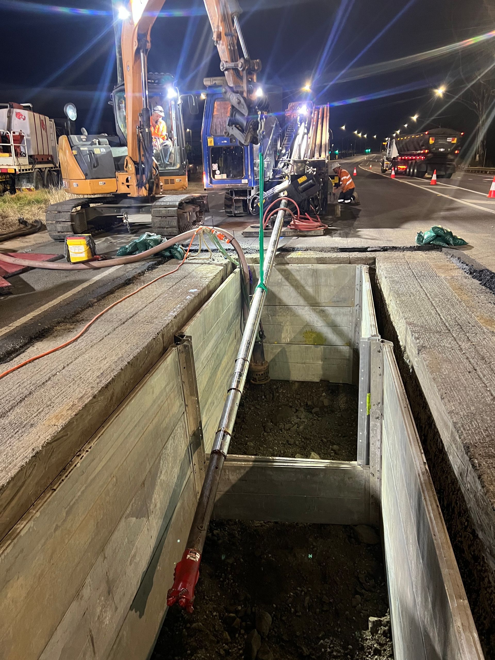 A drilling machine is operating on grassy ground near a truck, with water and mud splashing around