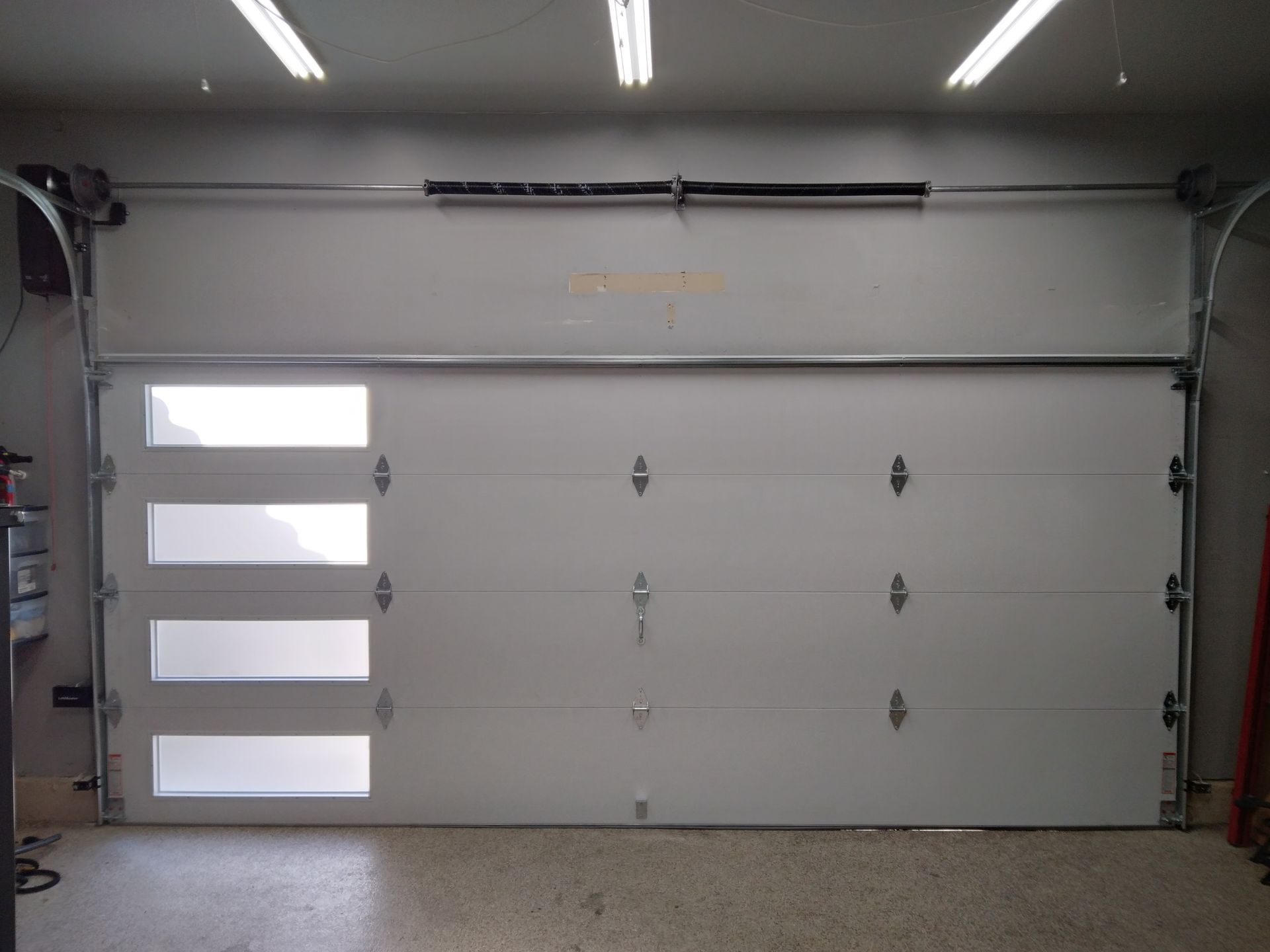 A white garage door with four windows is open in a garage.