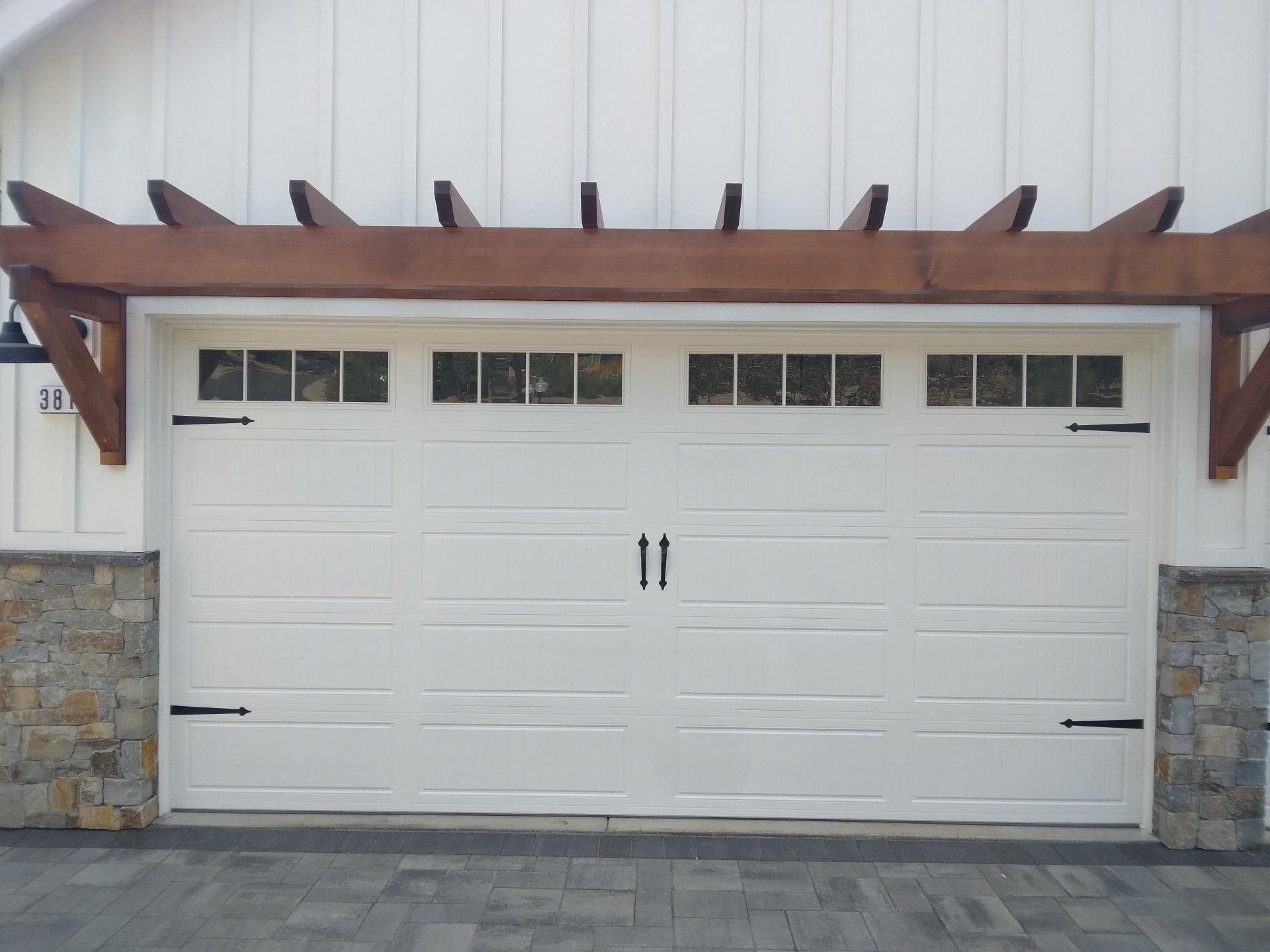 A white garage door with a wooden pergola over it.