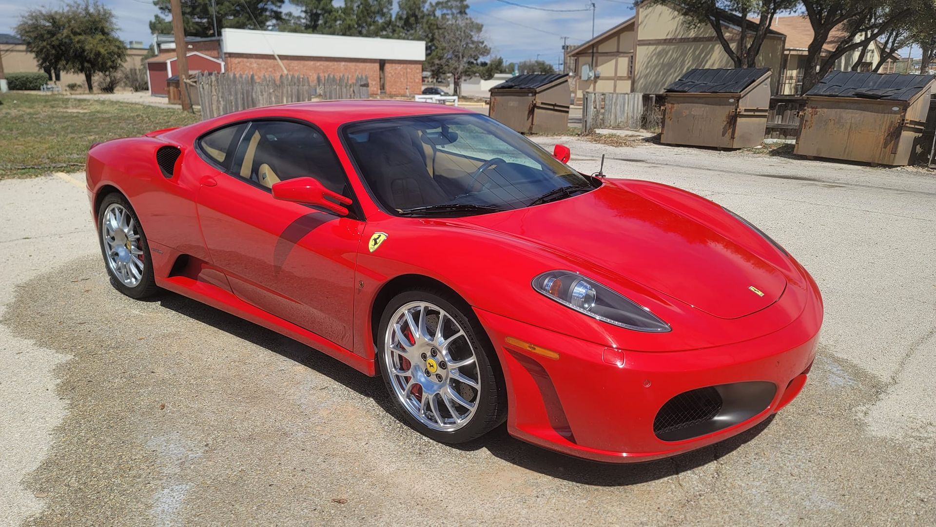 A red ferrari sports car is parked in a gravel lot.