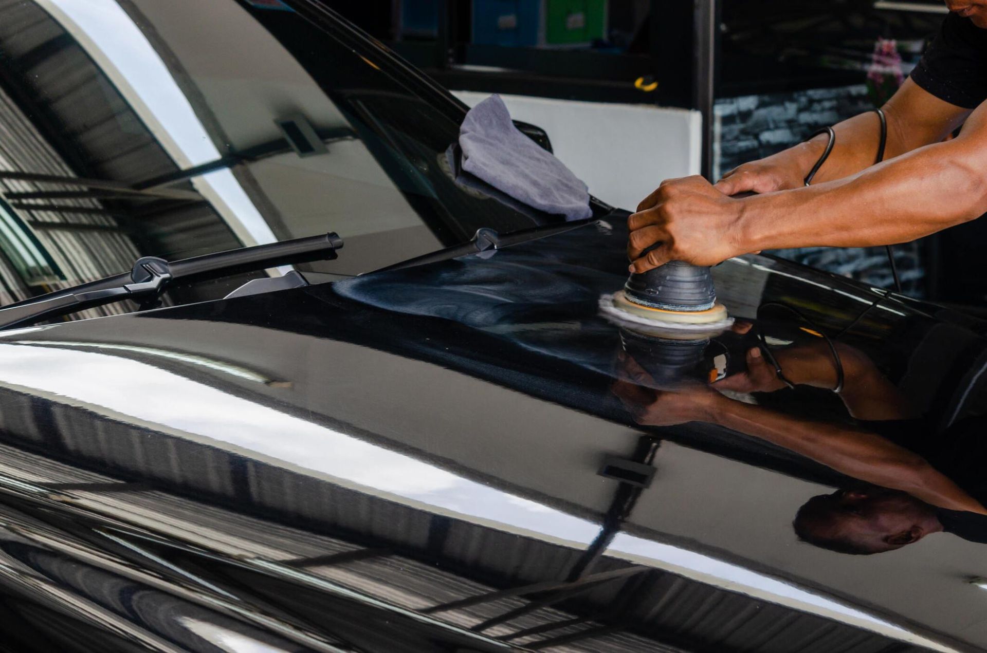 A man is polishing the hood of a black car.