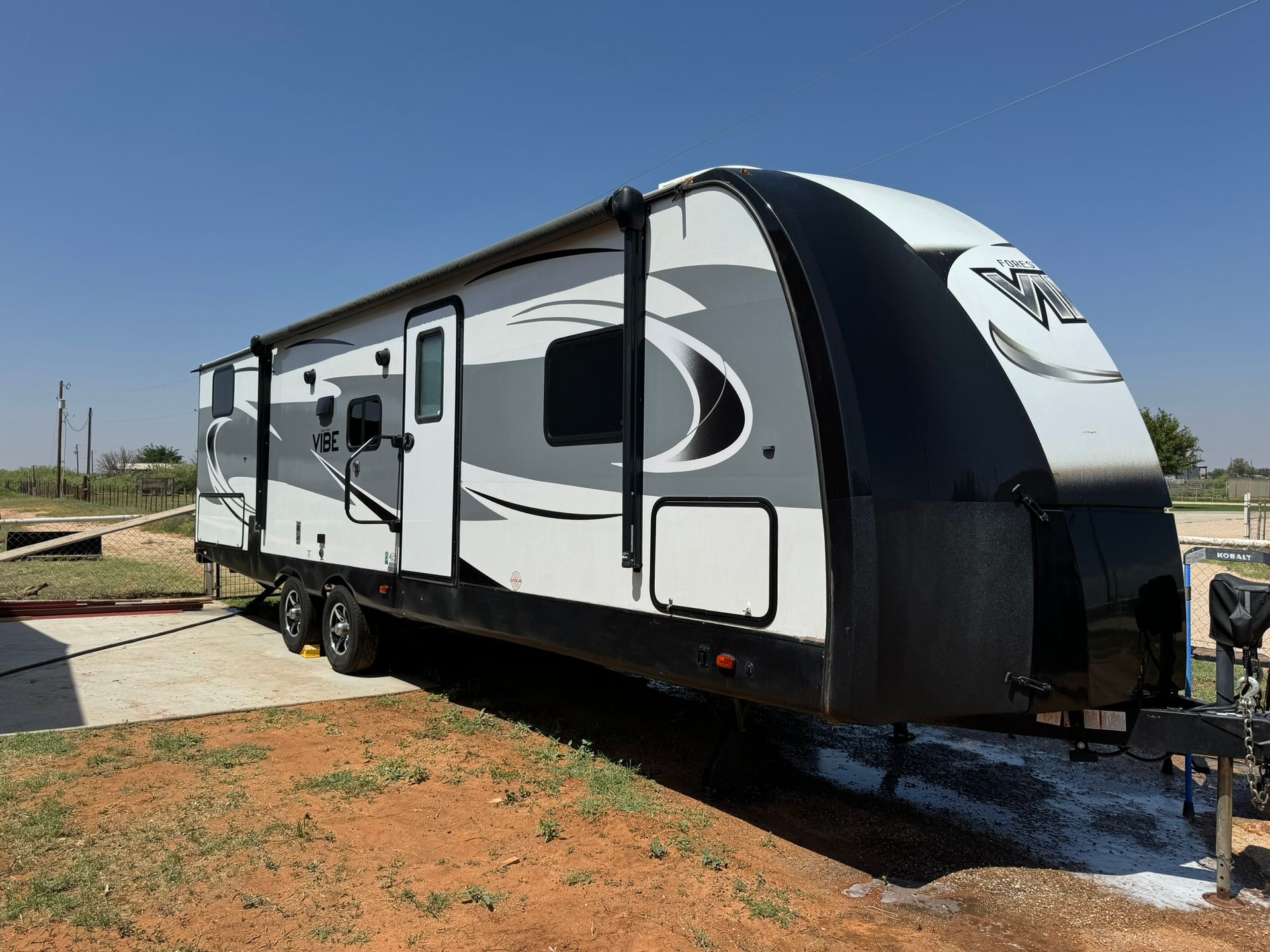 A white and black trailer is parked in a dirt field.