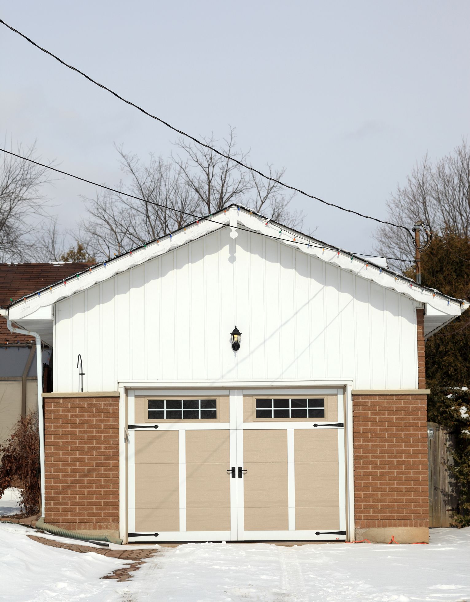 White garage with beige doors and brown brick base, in snow.