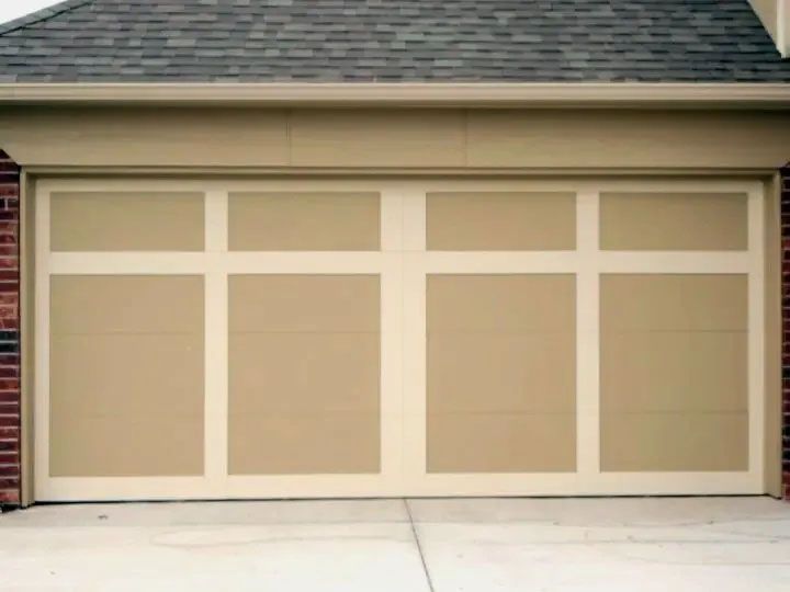 Tan garage door with a white grid design, in front of a driveway and brick siding.