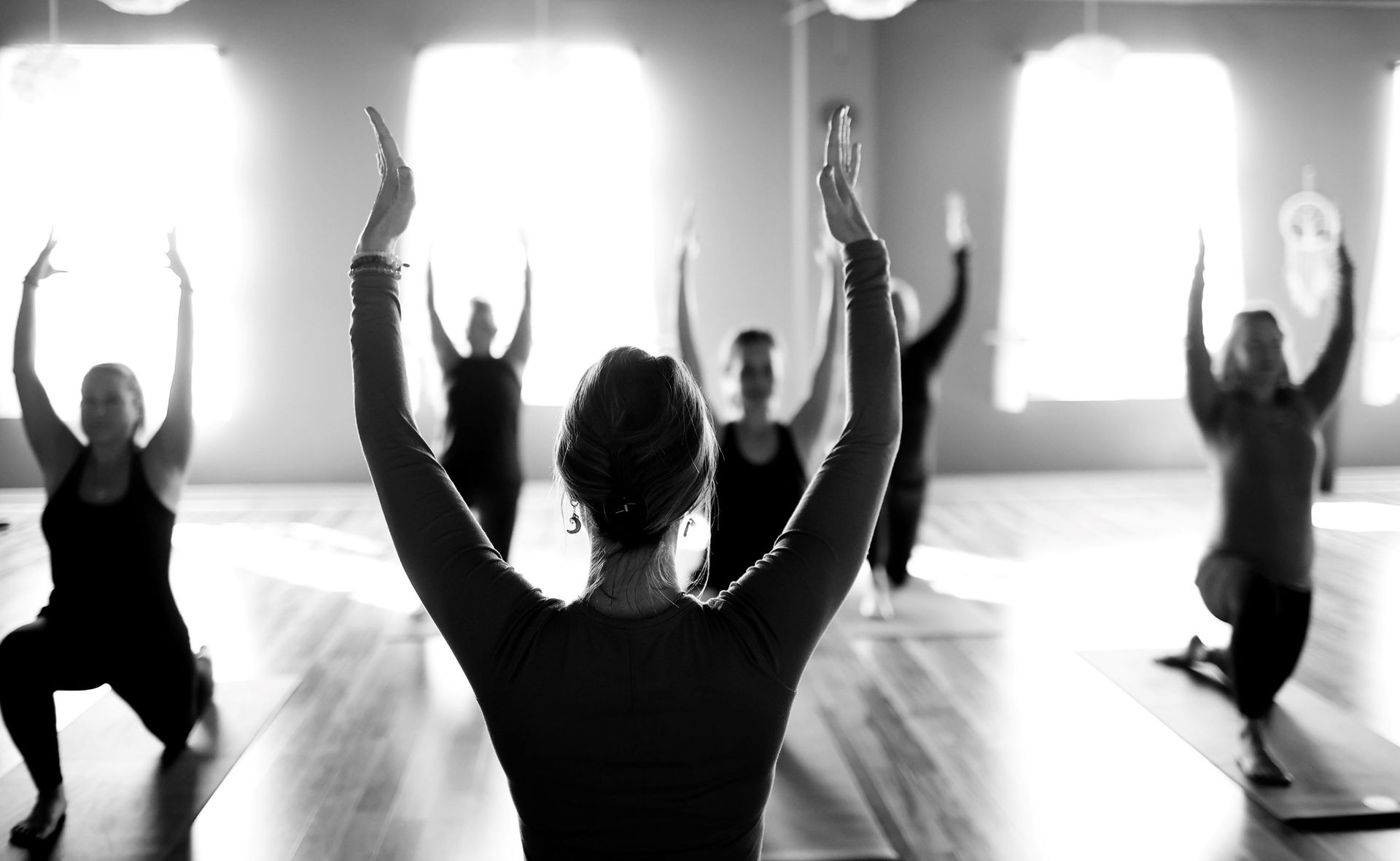 People in a yoga class, arms raised, in a brightly lit studio.