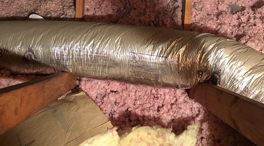A close up of a duct in an attic with pink insulation.