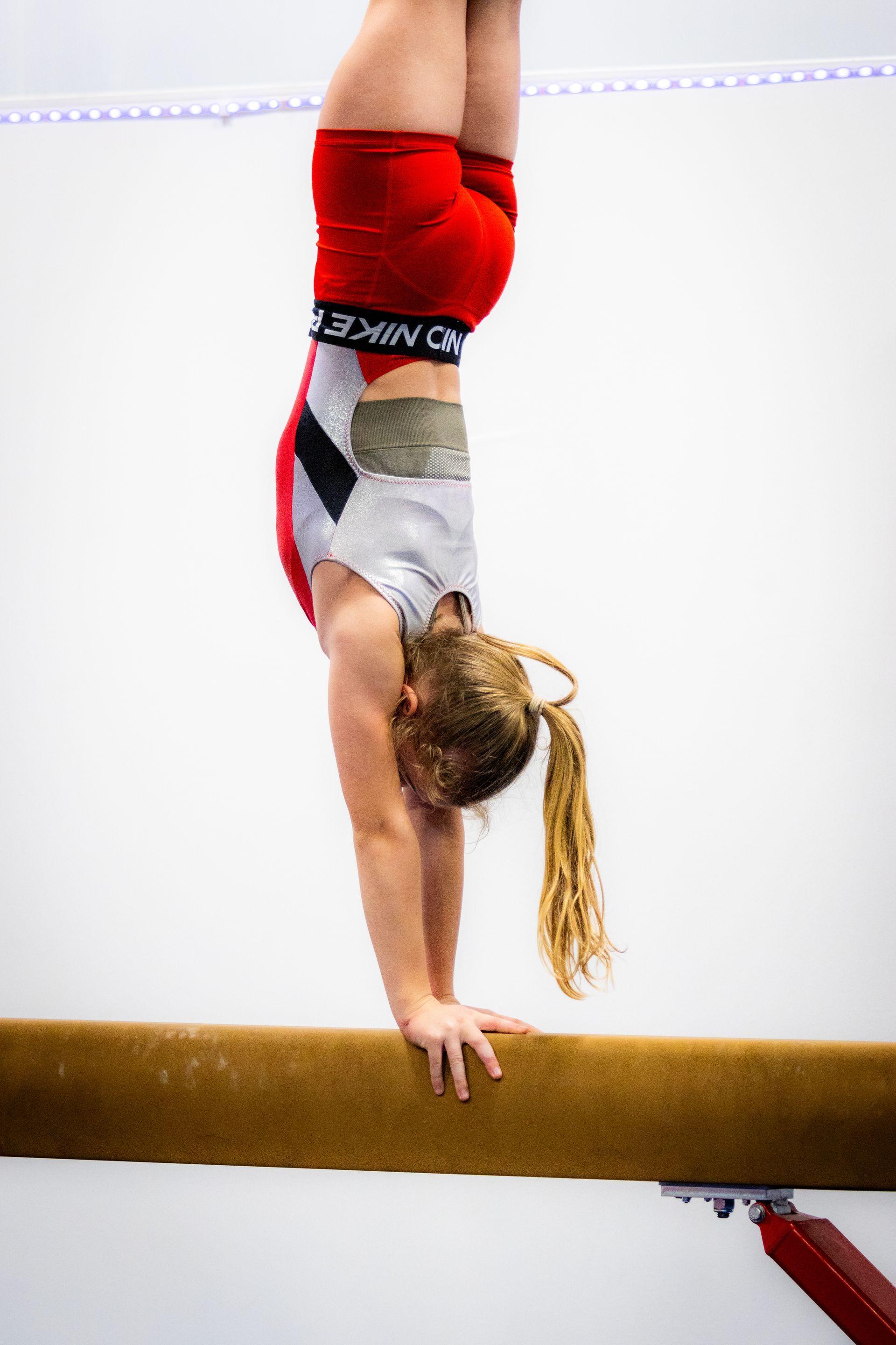 A female gymnast is doing a handstand on a balance beam.