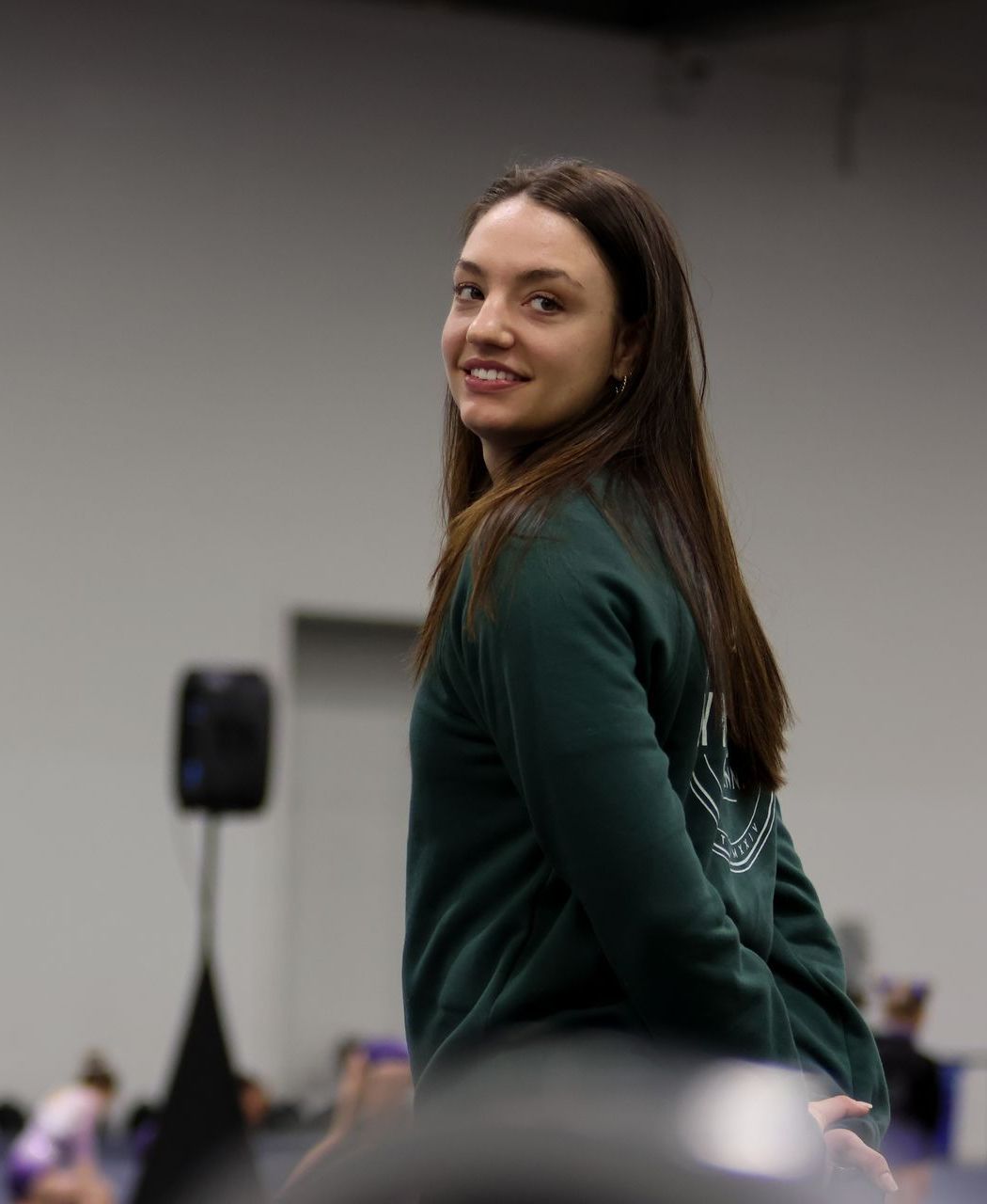 A woman in a green shirt is standing in a room and smiling.