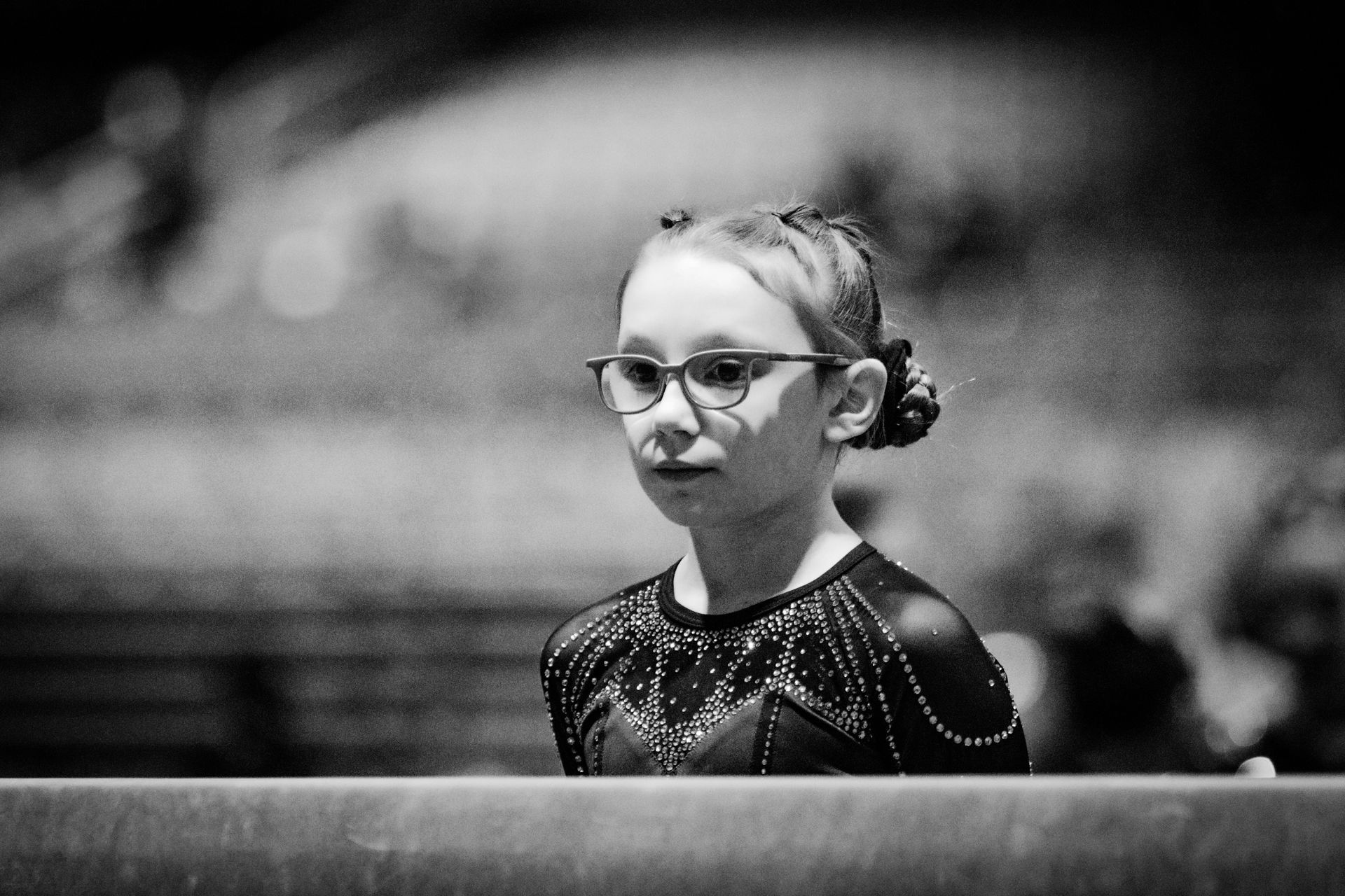 A young girl wearing glasses is standing on a balance beam in a black and white photo.