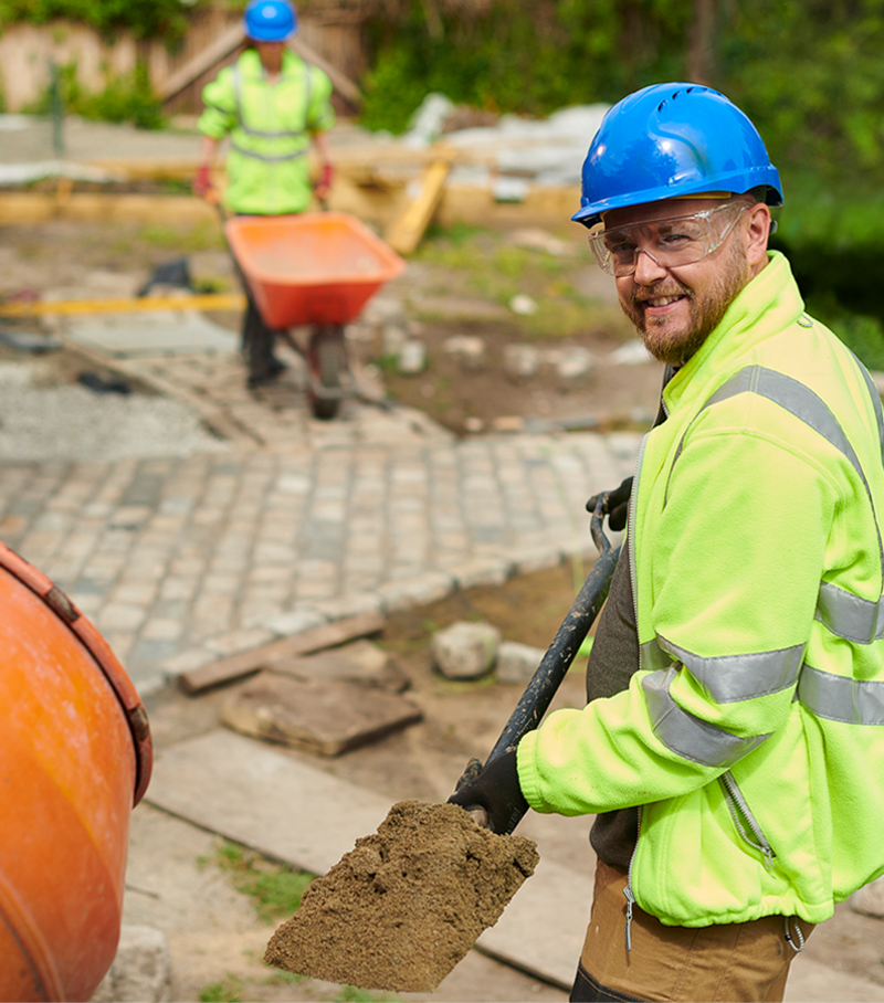 A man wearing a blue hard hat is holding a shovel.