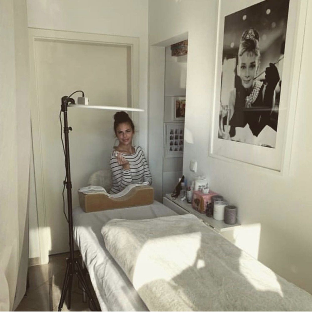Een vrouw zit op een bed in een kamer met een foto van Audrey Hepburn aan de muur.